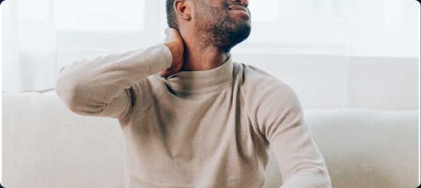 A man sitting on a couch and holding the back of his neck