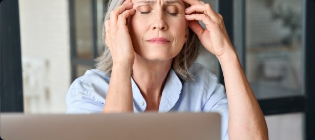 A woman at a laptop with her eyes closed and her fingertips at her temples